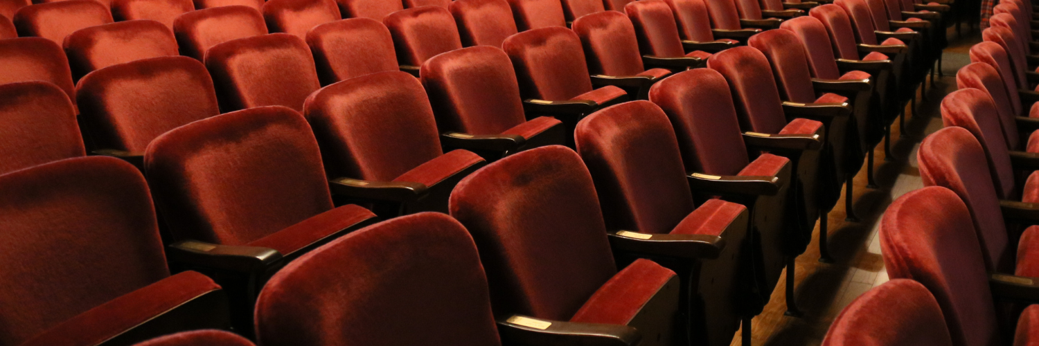 Rows of red seats in a theatre with brass seat plaques on the arm rests