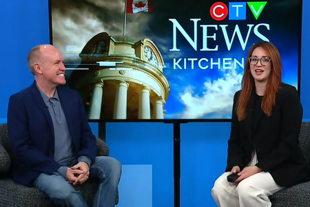 David Connolly and Daryl Morris sitting in front of a CTV News Kitchener backdrop. David wears a dark blue shirt and jeans, while Daryl on the right is dressed in a black blazer and white pants. Both are seated on grey upholstered chairs. The backdro<