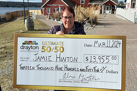 50/50 winner Jamie Hinton holding a big winner's cheque outside King's Wharf Theatre