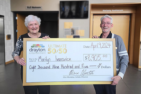 Marilyn Ivanovick and Gary Good hold a mock-up cheque in the foyer of Hamilton Family Theatre Cambridge<