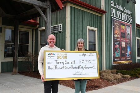 Two smiling individuals stand outside the St. Jacobs Country Playhouse, holding a large cheque made out to Tammy Barrett for $3,755.00 from Drayton Entertainment's 50/50 draw, dated April 4, 2025. The cheque is signed by David Connolly, Artistic Dire