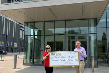 Tracie Settler (left) stands outside the Hamilton Family Theatre Cambridge holding a large presentation cheque for $5,655 alongside Drayton Entertainment Artistic Director David Connolly (right). The cheque, dated June 3, 2025, recognizes Tracie as t