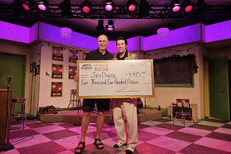 In this vibrant on-stage photo, Million Dollar Quartet actor Matt Cage, dressed as Elvis in a glittering gold jacket, presents a giant cheque to Jim Davey, the winner of Drayton Entertainment’s Ultimate 50/50 Draw. The cheque is made out for $4,415 a