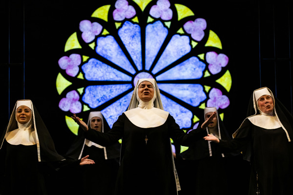 Performers standing in front of stained glass window and singing