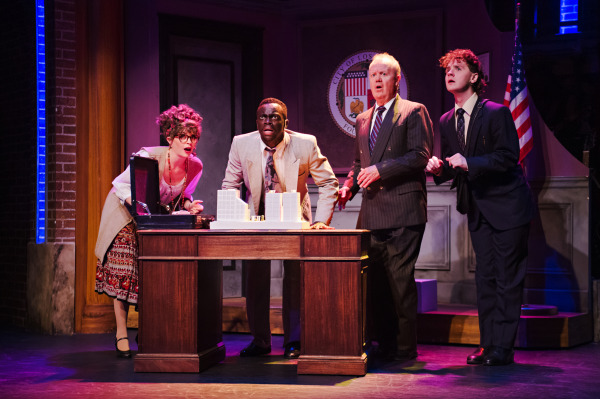 Production photo of Rock of Ages, showing four actors gathered around a table. They have shocked expressions. 