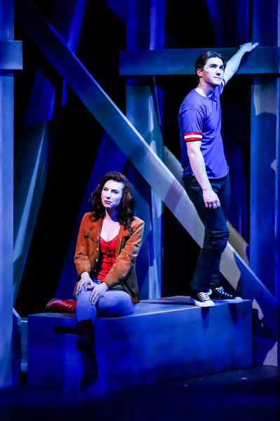 Production photo of Footloose showing a teen girl and teen boy standing on the set. 