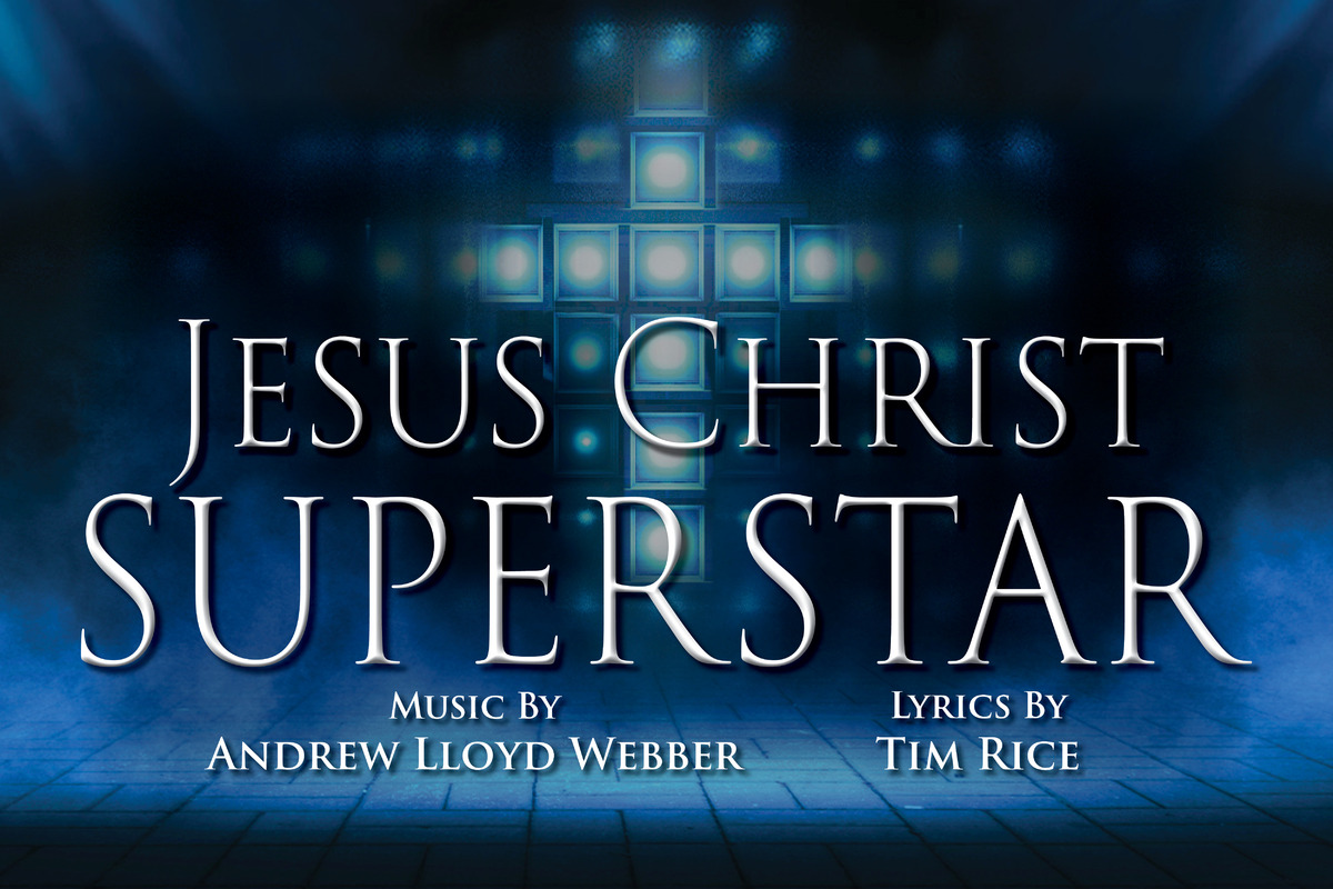 The promotional image for Jesus Christ Superstar features the title in bold, white letters against a sparkling, bokeh background. The backdrop transitions from brightly illuminating a cross outline in the center to shadow and smoke in the perimeter
